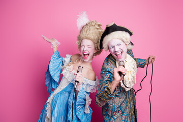 Young couple in vintage costumes enjoying a lively performance against a pink backdrop, celebrating historic theme party