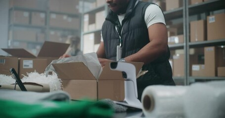 Close Up of African American Postal Worker, Shipping Clerk Packing Cardboard Parcel with E-Commerce Order, Scanning Code, Preparing Package for Delivery. Warehouse, Sorting Center of Postal Service.