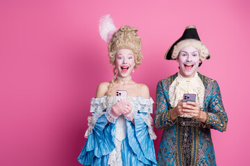 Charming young couple dressed in elaborate baroque costumes, posing joyfully against a vibrant pink background