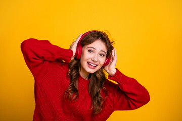 Young woman in headphones on yellow background enjoying music while wearing a red sweater and smiling joyfully