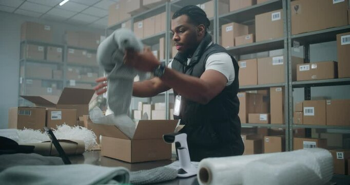 African American Warehouse Clerk Puts Sticker on Cardboard Box with Online Order, Prepares Parcels for Shipping, Scans Code, Uses Tablet Computer. Sorting Center of E-Commerce Store, Delivery Service.