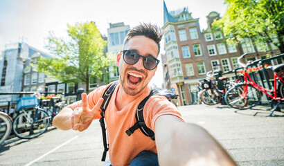 Happy tourist taking selfie picture in Amsterdam, Netherlands - Cheerful man using smart mobile phone device outside - Student traveler enjoying summer european vacation - Life style tourism concept