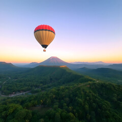 Naklejka premium A hot air balloon drifts above vibrant green mountains with a volcano in the soft light of dawn.