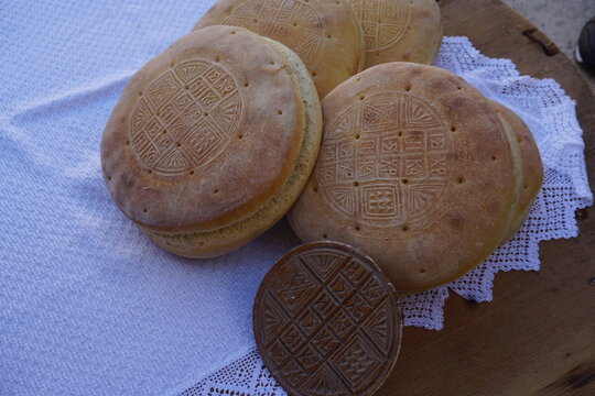 Many traditional handmade sourdough prosfora (altar breads) on a white towel on a wooden table - Embossed on them by the wooden stamp next to them is the message "Jesus Christ wins"
