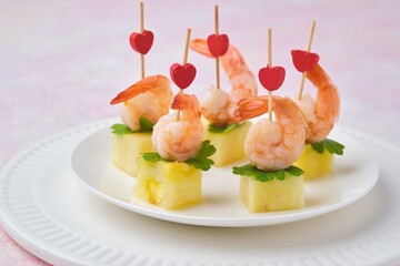 Appetizer of fresh pineapple cubes and shrimps marinated in sauce on a skewer on a white ceramic...