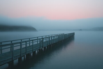Fototapeta premium Wooden dock on a still lake at dawn with soft pink hues