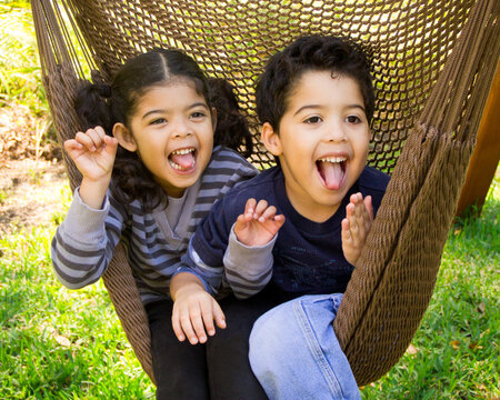 Close-up of a boy and girl sitting in a hammock  messing about pulling funny faces