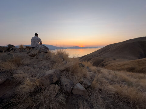 Rear view of a man sitting by the ocean watching the sunset over Lawa Darat Gili island, Komodo National Park, Indonesia