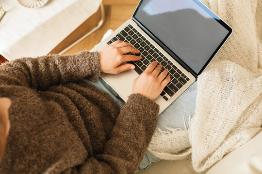 Overhead view of a woman sitting on a comfortable sofa in a living room using a laptop computer with a blank screen