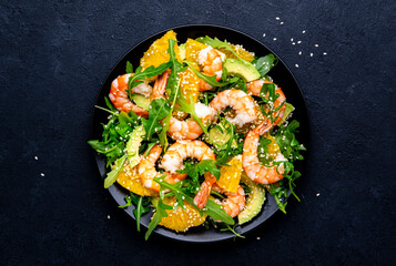 Yummy shrimp salad with avocado, orange, arugula and sesame seeds on black table background. Top view