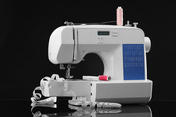 Sewing machine with measuring tape and spools of threads on black background