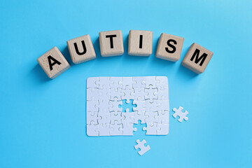 Word Autism made of wooden cubes and puzzle on light blue background, top view