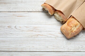 Paper bags with fresh baguettes on wooden table, top view. Space for text