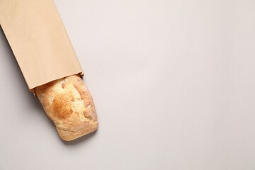 Paper bag with fresh baguette on light gray table, top view. Space for text