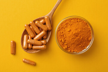 Many turmeric capsules and powder on yellow background, flat lay
