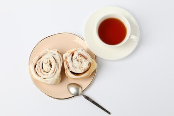 Delicious frosted cinnamon rolls and tea on white table, flat lay