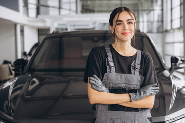 Portrait of young woman, professional female mechanic smiling at camera standing in auto repair shop. Car service, repair, maintenance and people concept.