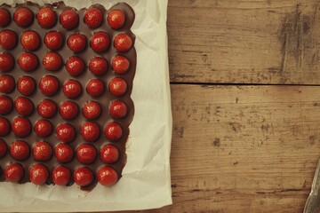 Fresh Strawberries Covered in Rich Chocolate Placed on a Parchment Paper Lined Baking Sheet Under Warm Indoor Lighting in a Rustic Kitchen Setting