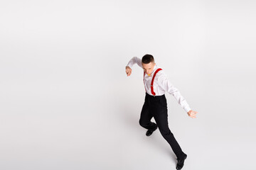 Young gentleman dancing energetically in elegant vintage style with red suspenders against a white...