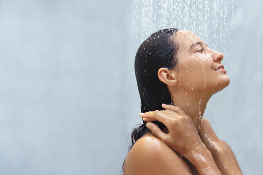 A serene woman with closed eyes enjoys the refreshing sensation of a gentle shower, her hands resting on her neck. This peaceful moment of self-care embodies concepts of relaxation, wellness, and