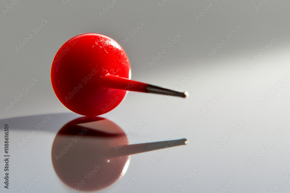Poster Close-up of a red pushpin lying on a reflective surface with soft light