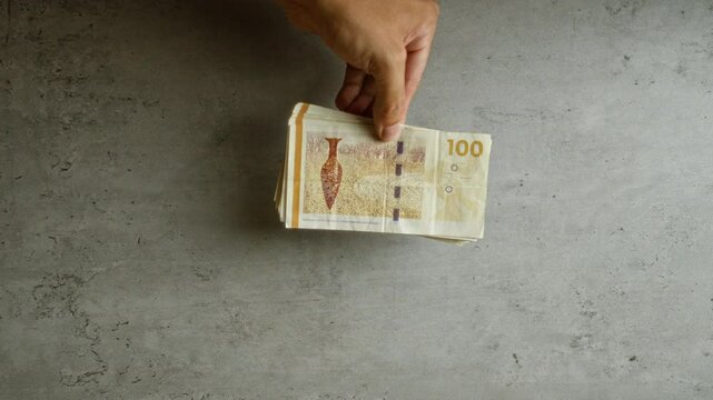 Hand holding danish 100 krone bills over a concrete surface, showcasing scandinavian currency in a simple background setting.