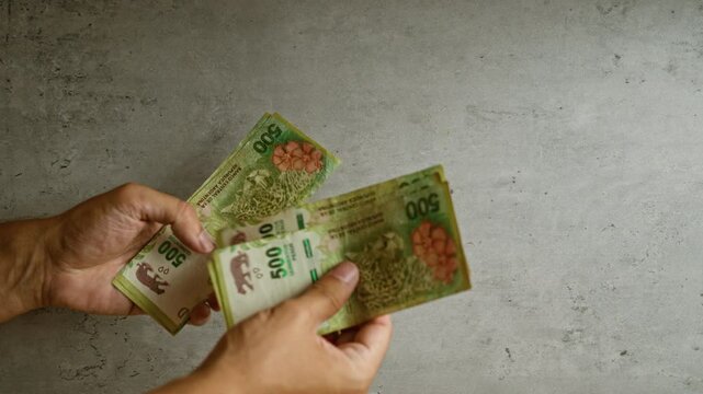 Man hands counting argentinian peso banknotes against a concrete background, highlighting fingertips and currency details with a subtle texture.