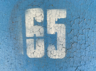 White number 65 on textured background with old cracked blue paint. Sixty-five