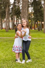 Two young girls are standing in a grassy field, hugging each other