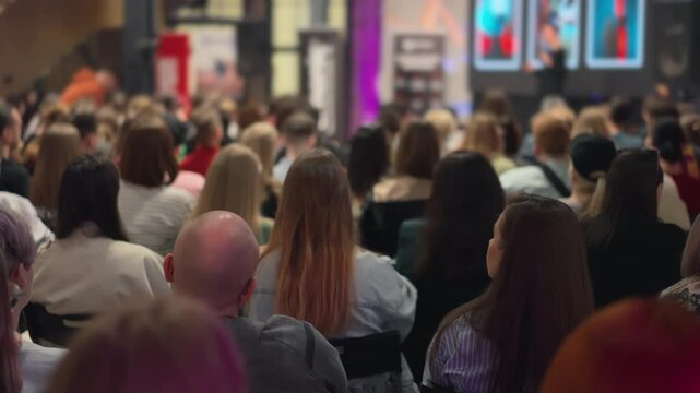 Creators partake in self-improvement lecture, speaker and presentation blurred in distance. Youthful gathering emphasizing personal growth in arts. Suitable for depicting creative development sessions