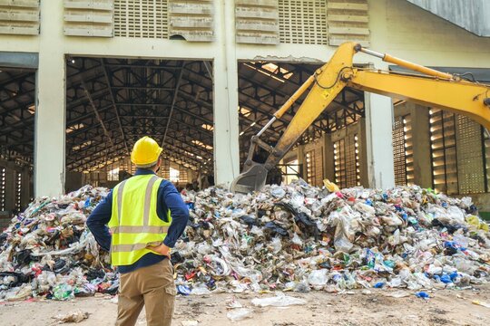 A environmental engineers are checking the quality of waste in a waste sorting plant with a backhoe in the background.