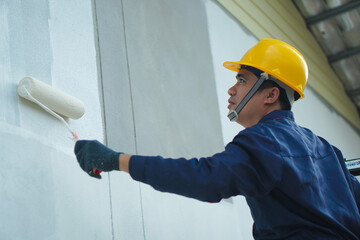 Asian construction worker painting the walls of a house outdoors