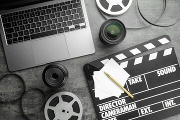 Flat lay composition with movie clapper, film reels and camera lens on grey textured table