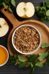 Delicious apple crisp in bowl, fresh fruits, honey and mint on black textured table, flat lay