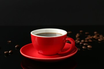 Red cup with coffee and roasted beans on black background