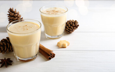 Tasty Christmas cocktail (eggnog) in glasses, pine cones and spices on white wooden table, closeup. Space for text