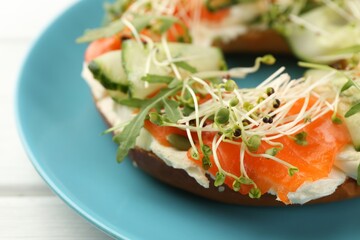 Half of delicious bagel with salmon, microgreens, arugula and cream cheese on white wooden table, closeup