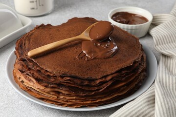 Delicious chocolate crepes with sweet paste on light grey table, closeup
