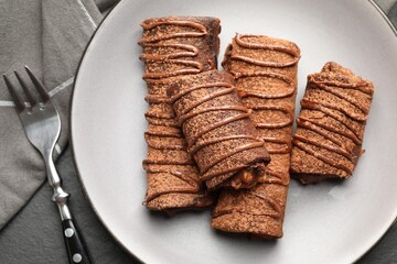 Delicious chocolate crepes with sweet paste and nuts on black table, top view