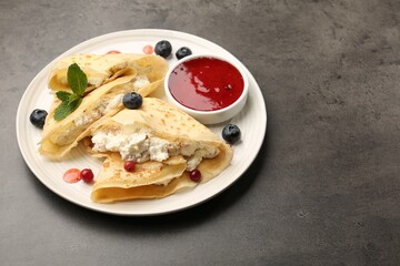 Delicious crepes with cottage cheese, jam, redcurrants and blueberries on grey table