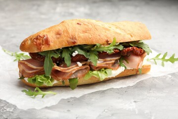 Obraz premium Baguette sandwich with ham and sun dried tomatoes on grey textured table, closeup