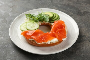 Delicious bagel with salmon, cream cheese, cucumber and avocado on grey table, closeup