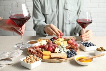 Women holding glasses of wine at light grey table with different snacks indoors, closeup
