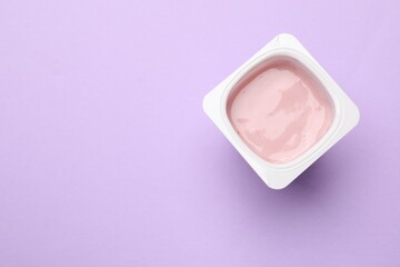 Delicious yogurt in plastic cup on violet background, top view. Space for text