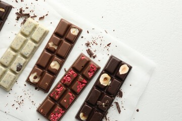 Tasty chocolate bars and crumbs on white textured background, flat lay. Space for text