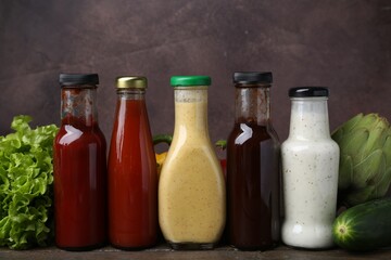 Tasty sauces in glass bottles and fresh products on wooden table, closeup
