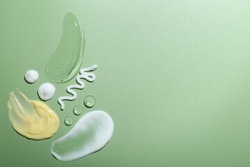 Cream and gel samples on green background, top view. Space for text