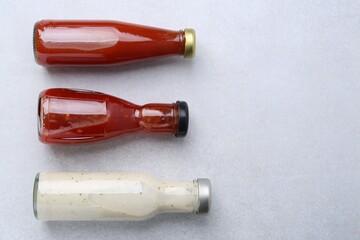 Tasty sauces in glass bottles on white table, flat lay. Space for text