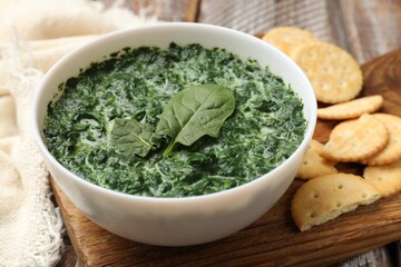 Delicious spinach sauce in bowl and crackers on table, closeup