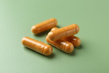 Many turmeric capsules on light green background, closeup